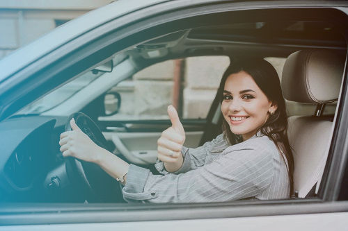 kobieta w szarej koszuli prowadzi samochod i jest zadowolona oraz pokazuje gest okej